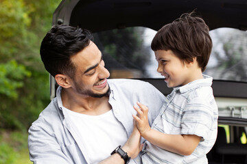 Portrait Of Happy Arab Man And His Little Son Standing Near Car With Open Trunk, Cheerful Young Middle Eastern Father Holding Male Child, Relaxing And Bonding Outdoors Together, Enjoying Family Trips