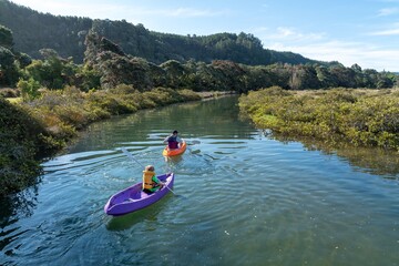 Father and son kayaking on a sunny day through a tranquil waterway. Nature surrounds them with lush greenery. Family fun. Opoutere, Whangamata, Coromandel Peninsula, New Zealand