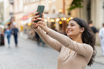 Indian young woman blogger taking selfie on smartphone, communicating video call online with...