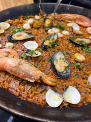 Traditional Paella served at restaurant seafood paella in the fry pan with a huge iron spoon, shrimp and mussels, lemon