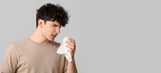 Young man with runny nose on grey background with space for text. Allergy concept
