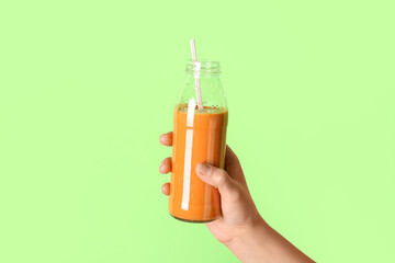 Female hand with glass bottle of orange smoothie on green background