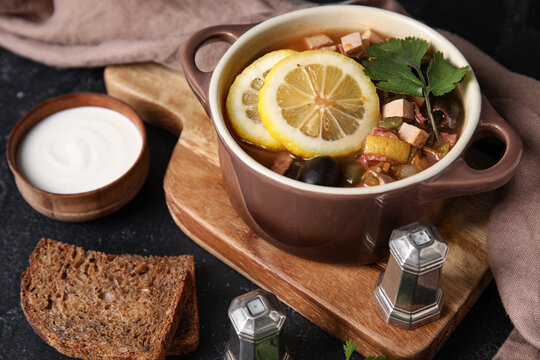Pot of tasty Hodgepodge soup with bread and sour cream on dark background