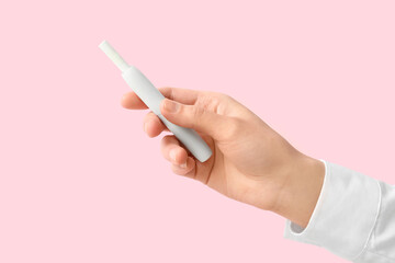 Female hand holding modern electronic cigar with stick on pink background
