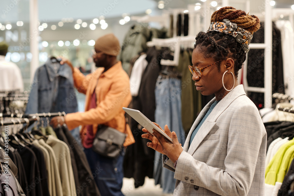Aufkleber Young elegant shop assistant in eyeglasses and suit looking at tablet screen while scrolling through online items