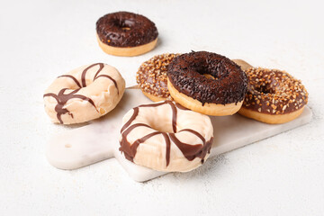 Board with sweet chocolate donuts on light grunge background