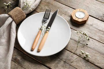 Plate with folded napkin, cutlery and candle on brown wooden background