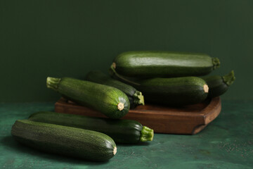 Wooden board with many fresh zucchini on green table