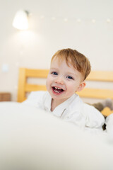 Naklejka premium Happy child playing in a cozy bedroom. A smiling child enjoys playful moments on a soft bed in a bright and cozy bedroom, radiating joy and innocence.