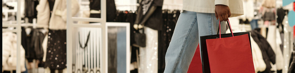 Header of hand and legs of young contemporary female consumer with shopping bags moving along large...