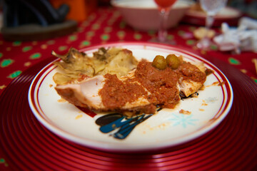 A festive close-up of turkey slices with sauce on a red Christmas tablecloth, creating a warm, holiday dining atmosphere.