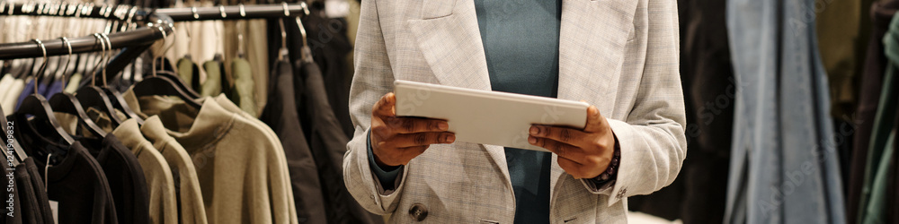Aufkleber header of young elegant female shop assistant in white blazer using tablet while standing in front o