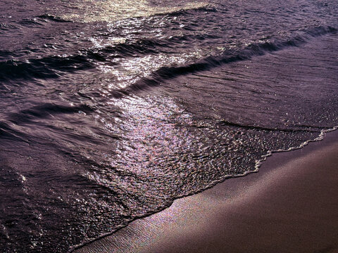 Glittering sea waves on sandy beach at night.