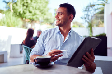 Young business professional enjoying a coffee while using digital tablet and stylus at outdoor cafe