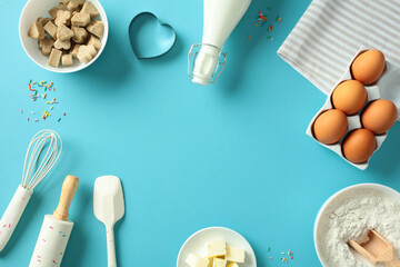 Baking essentials on a blue background: eggs, flour, butter, milk, sugar cubes, whisk, rolling pin,...