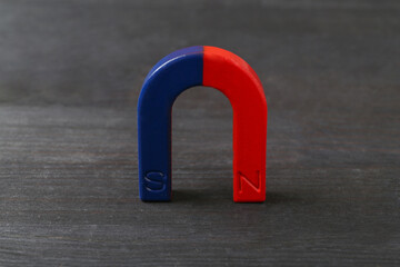 One horseshoe magnet on black wooden table, closeup