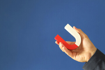 Man holding horseshoe magnet on blue background, closeup. Space for text