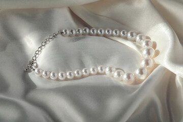 Beautiful pearl necklace on white silk, closeup