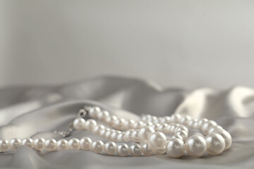 Beautiful pearl necklace on white silk, closeup. Space for text