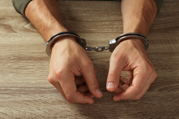 Man in metal handcuffs at wooden table, closeup