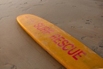Yellow surf rescue board on a sandy beach, lifeguard equipment.