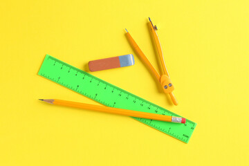 Ruler, pencil, compass and eraser on yellow background, flat lay