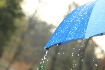 Open blue umbrella under pouring rain outdoors, closeup. Space for text