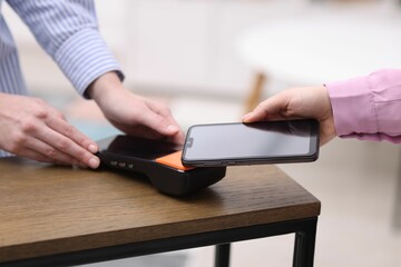 Woman paying with smartphone via terminal at wooden counter indoors, closeup