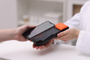 Woman paying with smartphone via terminal at counter indoors, closeup