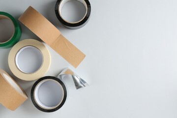 Rolls of different adhesive tapes on white background, flat lay. Space for text