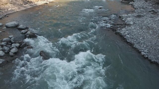 Fast moving stream of seething mountain river runs along stone banks. Altai