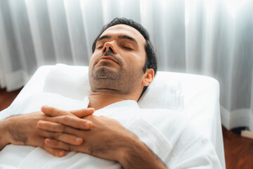 Caucasian man customer enjoying relaxing anti-stress spa massage and pampering with beauty skin recreation leisure in day light ambient salon spa at luxury resort or hotel. Quiescent