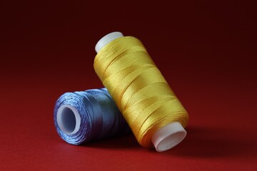 Spools of colorful sewing threads on red background, closeup