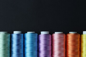 Spools of colorful sewing threads on black background, flat lay. Space for text