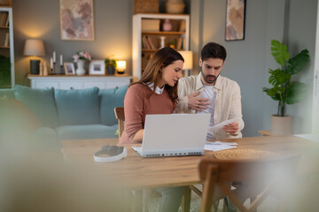 Young stressed Caucasian couple facing financials troubles, sitting at kitchen table with papers