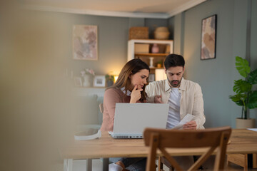 Young stressed Caucasian couple facing financials troubles, sitting at kitchen table with papers