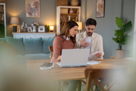 Young stressed Caucasian couple facing financials troubles, sitting at kitchen table with papers