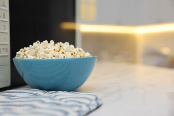 Tasty popcorn in bowl near microwave oven on white table indoors, space for text