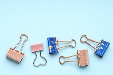 Different binder clips on light blue background, flat lay. Space for text