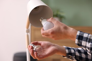 Man changing incandescent light bulb for fluorescent one in lamp at home, closeup