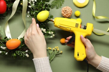 Woman with hot glue gun making craft on olive background, top view