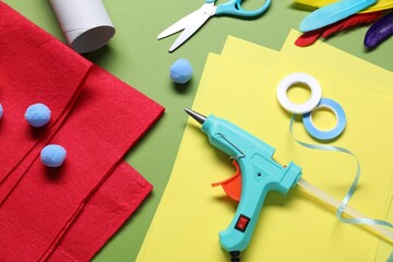 Hot glue gun and handicraft materials on green background, flat lay