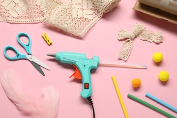 Hot glue gun and handicraft materials on pink background, flat lay