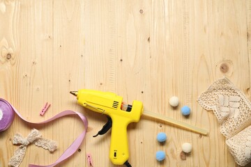 Hot glue gun and handicraft materials on wooden background, flat lay. Space for text