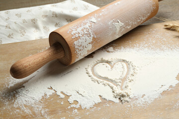 Rolling pin and heart shape made of flour on table, closeup