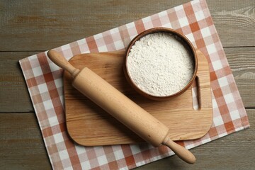 Rolling pin, bowl of flour and board on wooden table, top view