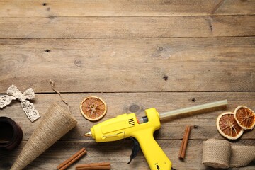 Hot glue gun and handicraft materials on wooden background, flat lay. Space for text