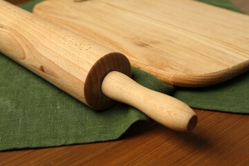 Rolling pin and green napkin on wooden table, closeup