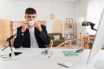 Male podcaster drinking coffee at table in studio