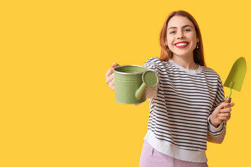 Beautiful young woman with watering can and gardening shovel on yellow background